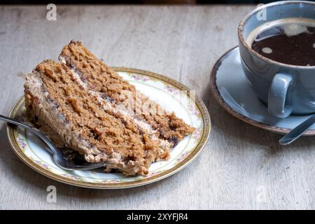 UK A single serving or slice of coffee and walnut cake werved plated with a small fork. The cake is served on a table with a fresh cup of black coffee Stock Photo