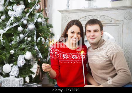 Young happy couple sitting by Cristmas tree holding Bengal fire Stock Photo