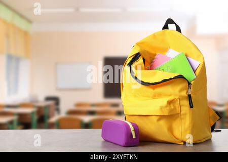 Yellow backpack with stationery on school desk in classroom. Space for text Stock Photo