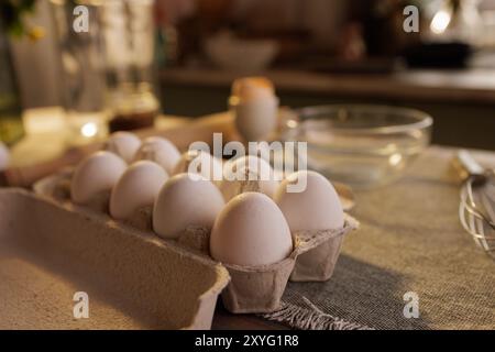 A close-up of a carton of white eggs on a kitchen countertop, with a blurred background showing a person and kitchen utensils Stock Photo