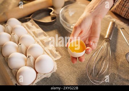Close-up of female hands holding broken chicken egg on kitchen table background, egg carton, dough preparation Stock Photo