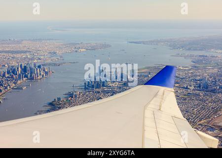 View from airplane window with wing visible, showing Manhattan's skyscrapers and the Hudson River below. New York. USA. Stock Photo