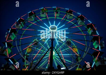 ARLINGTON, Virginia — A vibrantly illuminated Ferris wheel stands out against the twilight sky at the Arlington County Fair. The wheel's colorful lights create a dazzling display, capturing the festive atmosphere of the fair as day turns to night. This iconic carnival ride serves as a centerpiece for the annual community event, offering both thrilling views for riders and a picturesque scene for fairgoers. Stock Photo