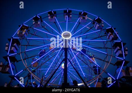 ARLINGTON, Virginia — A vibrantly illuminated Ferris wheel stands out against the twilight sky at the Arlington County Fair. The wheel's colorful lights create a dazzling display, capturing the festive atmosphere of the fair as day turns to night. This iconic carnival ride serves as a centerpiece for the annual community event, offering both thrilling views for riders and a picturesque scene for fairgoers. Stock Photo