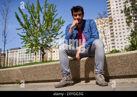young man sitting on a stone bench in the city looking at camera Stock Photo