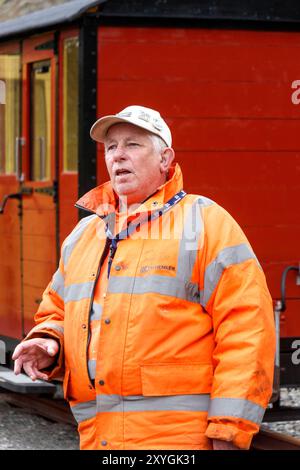 Railway worker in an orange safety jacket standing in front of a red train carriage. threlkeld quarry mining museum cumbria uk Stock Photo