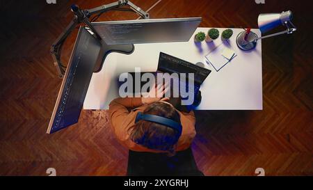 Top down view of engineer typing code in home office, using Java programming language to develop software application. It specialist using multimonitor PC setup and laptop to finish tasks, aerial shot Stock Photo