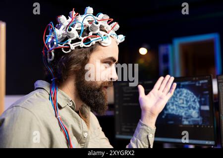 Smiling software technician using EEG headset to upload consciousness into computer. Happy IT admin working with AI, using high tech gear to create connection between brain and PC Stock Photo