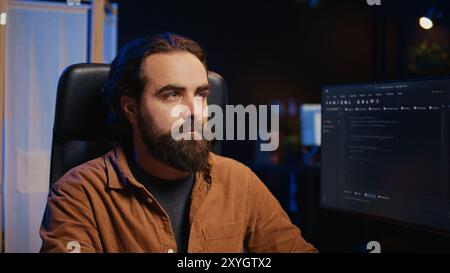 Developer overthinking solutions while doing programming during remote job shift in home office while drinking coffee. IT admin enjoying hot beverage working on PC early in the morning, camera B Stock Photo