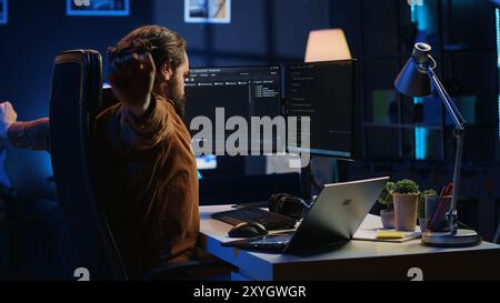 Tired software engineer taking break from coding, removing headphones, rubbing eyes, feeling exhausted. Drowsy IT admin drained by project overdue deadline, pausing tasks to rest Stock Photo