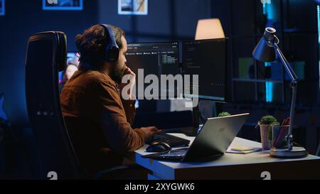 Hyperactive software developer suffering from adhd affliction, writing code, drinking coffee, listening music, arranging desk objects. Distracted IT admin doing multitasking in home office, camera A Stock Photo