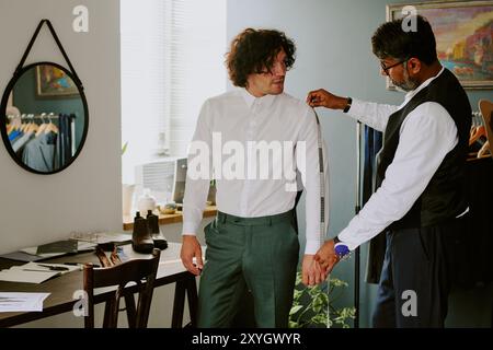 Professional tailor doing measurements while customer trying on fashionable suit Stock Photo