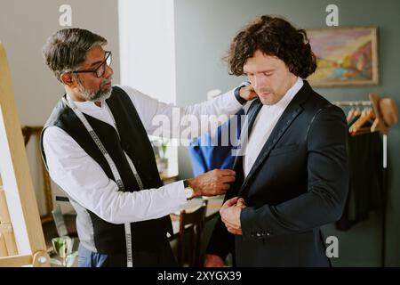 Indian tailor adjusting suit while customer looking at costume in atelier Stock Photo