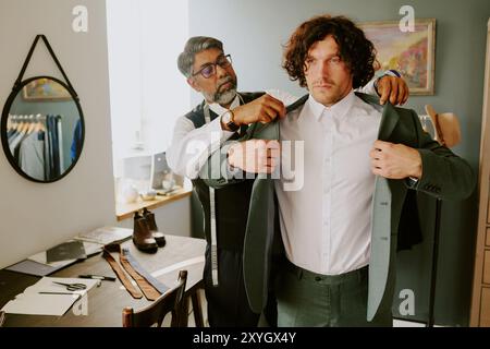 Brutal curly haired model trying on new suit while tailor assisting him Stock Photo