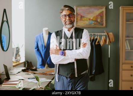 Professional tailor with crossed arms smiling and looking at camera while working in atelier Stock Photo