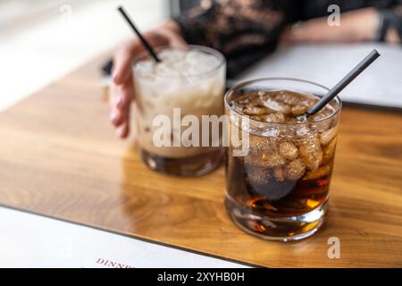 Two cocktail drinks on a wood table with a woman’s hand. Romantic dinner date night at a classy restaurant Stock Photo