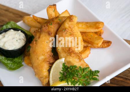 Serving of traditional fish and chips on a white plate with tartar sauce and a lemon wedge Stock Photo