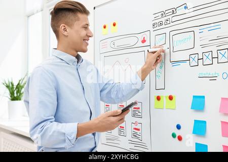 Developing UI design. Man drawing website wireframe on whiteboard indoors Stock Photo