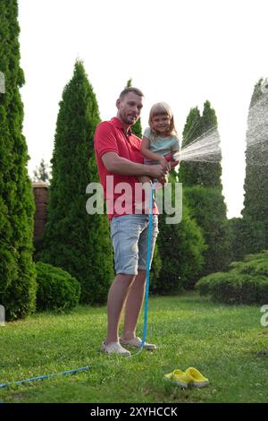 Father and his daughter watering lawn with hose in backyard Stock Photo