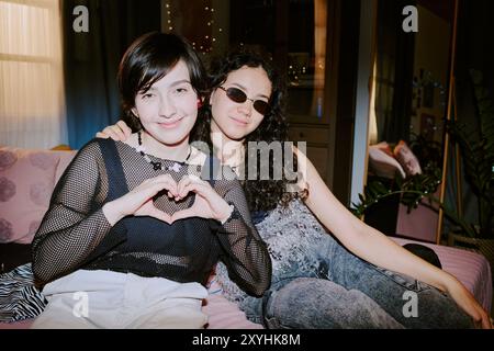 Portrait of Two Smiling Friends Making Heart Gesture Stock Photo