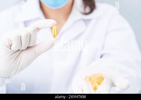 Close up Scientist hands putting in nitrile latex gloves holding Omega 3 capsule in labcoat wearing nitrile gloves, doing experiments in lab Stock Photo
