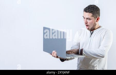 Amazed handsome man standing using laptop isolated. Surprised guy holding and looking at an promotion on laptop screen Stock Photo