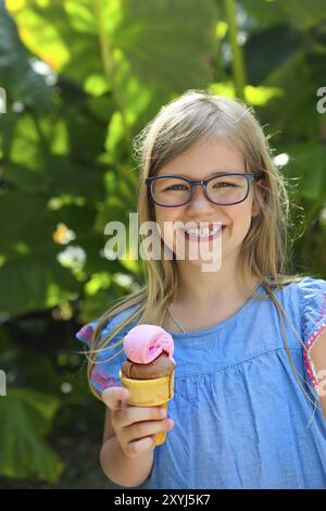 Portrait of the cute little girl with funny expression holding ice cream cone outside against bright nature background Stock Photo