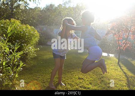 Child playing with garden sprinkler. Kids run and jump. Summer outdoor water fun in the backyard. Children play with hose watering flowers. Kids splas Stock Photo