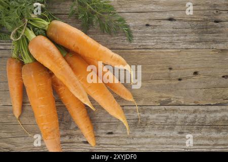 Bundle of vibrant orange carrots with green leafy tops is neatly tied together using twine and positioned on an old, rustic wooden table Stock Photo