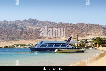 Two boats at the surf on the background of the beach with palm trees and high rocky mountains in Egypt Stock Photo