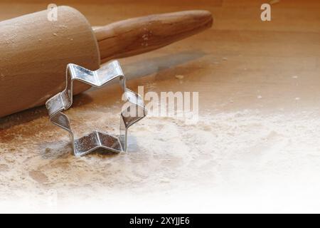 Christmas baking background, rolling pin and cookie cutter in star shape, some flour on warm wood, copyspace Stock Photo