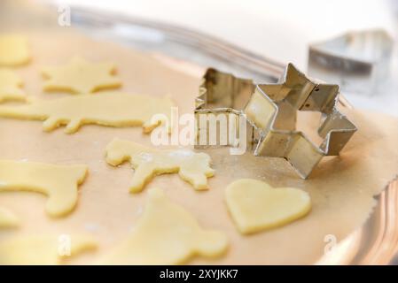 Christmas biscuits cut out in front of baking with cookie cutters in traditional shape. Draped on an antique silver tray with baking paper. Dough for Stock Photo
