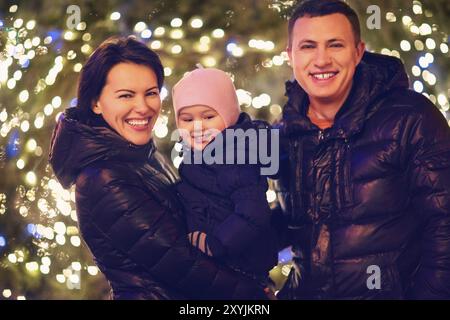 Happy family with little daughter looking at camera outside over Christmas background Stock Photo