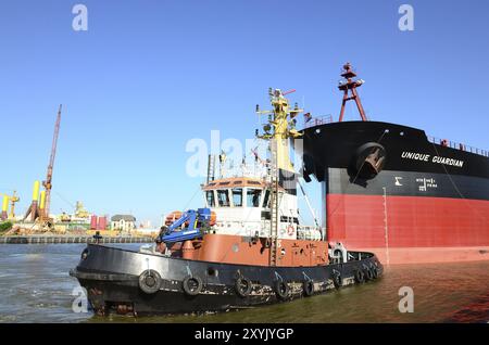 The oil tanker Unique Guaridan is towed in the harbour basin by a tugboat. Oil tanker towaged in harbour Stock Photo