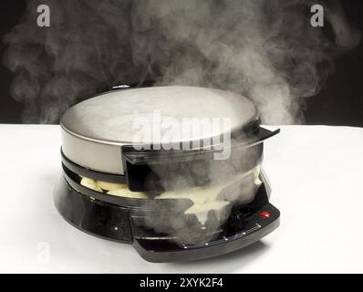 Making fresh steaming hot waffles with a waffle maker towards black on white Stock Photo