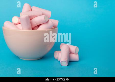 A horizontal image showing a close-up of a pink bowl filled with fluffy marshmallows, with an extra pile positioned on the left. The background is a c Stock Photo