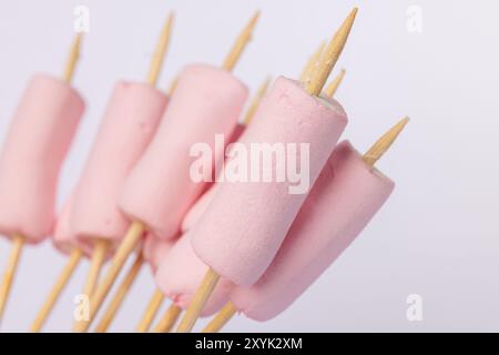 Horizontal image showing skewers with marshmallows, placed on the left side of a white backdrop. The marshmallows are in perfect alignment for toastin Stock Photo