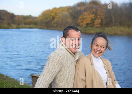 Young couple in love chilling by autumn lake. Happy man and woman enjoying nature and hugging. Romantic date Stock Photo