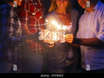 Young people with sparklers having fun on night outdoor party Stock Photo