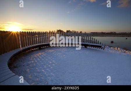 Sunbeams at sunrise over wooden bench in winter Stock Photo