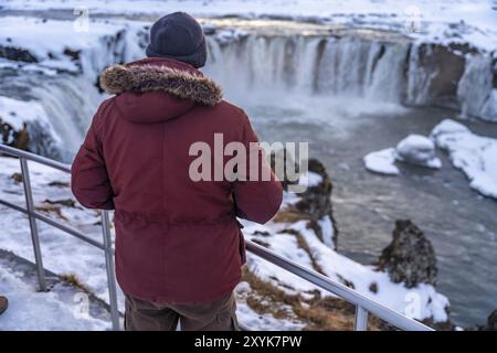 A male hiker looking at frozen Godafoss waterfall at sunset in winter, Iceland, Europe Stock Photo