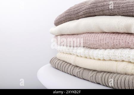 Stack of cozy knitted sweaters or blankets pastel trending colors on white modern chair against the wall Stock Photo