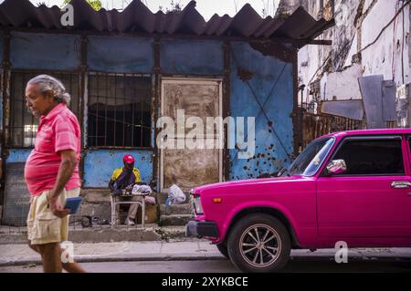 Havana, Cuba on December 23, 2015: A man walks down a street in Centro Habana with his shirt matching the color of a pink oldtimer Stock Photo