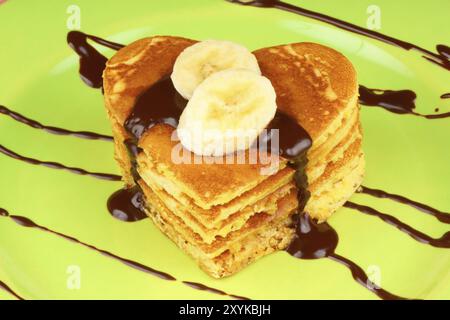 Heart shaped pancakes with chocolate sauce and banana slices on a green dish. A perfect breakfast for Valentine's Day Stock Photo