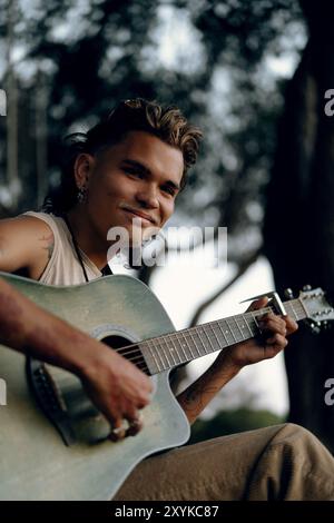 A young man plays a guitar in the park at sunset. Stock Photo