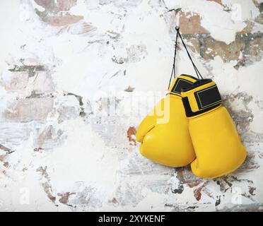 Pair of yellow boxing gloves hanging on a brick wall Stock Photo