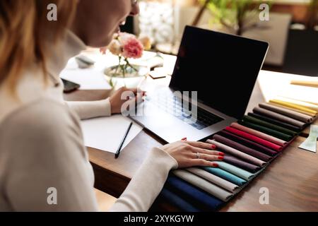 An interior designer is working on a new project. Choosing color from fabric color palette for new furniture. Oak wooden table. Cup of coffee, Flowers Stock Photo