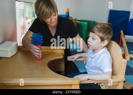 Young boy with neurodevelopmental disorders works on physical rehabilitation exercises with a therapist in a supportive therapy space designed for lea Stock Photo