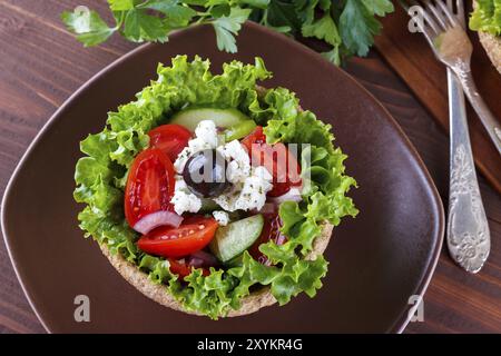 Greek salad in a bowl of whole-grain bread on wooden table, selective focus Stock Photo