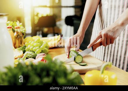 Close up on housewife woman, girl hands slicing cucumber at kitchen on chopping board. Female making healthy low calories salad, prepare green detox s Stock Photo